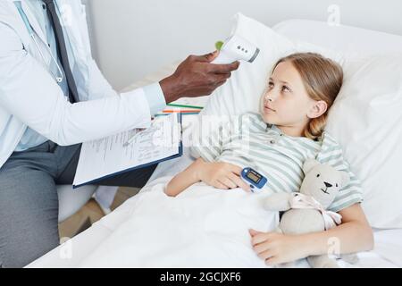 Ausgeschnittene Aufnahme eines Arztes, der die Temperatur des Kindes im Krankenhaus mit einem Infrarot-Thermometer überprüft, Platz kopieren Stockfoto