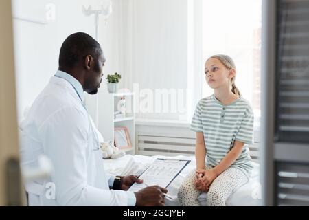 Porträt eines Teenagers, der mit dem Arzt spricht, während er im Krankenhauszimmer auf dem Bett sitzt Stockfoto