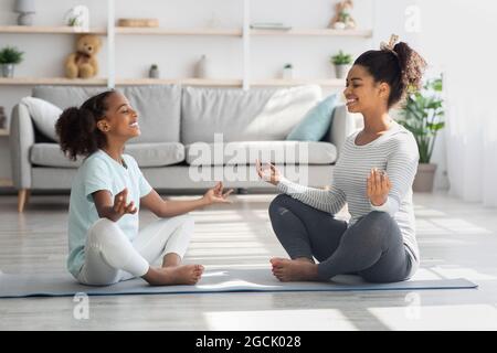 Sportliche schwarze Familie Mutter und Tochter meditieren zu Hause Stockfoto