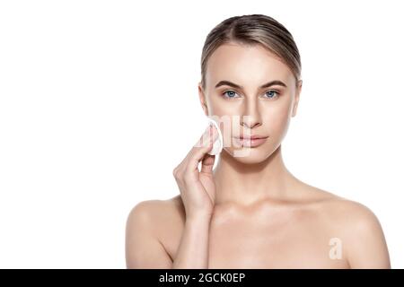 Schöne Frau mit Wattepad Make-up zu entfernen, Blick auf die Kamera lächelnd. Studio auf weißem Hintergrund aufgenommen. Beauty- und Hautpflegekonzept. Stockfoto