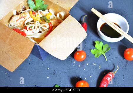 Nudeln mit Schweinefleisch und Gemüse in Take-out-Box auf Holztisch Chinesische Nudeln mit Gemüse. Zutaten in der Box: Nudeln, Hühnerfleisch, Pilze Stockfoto