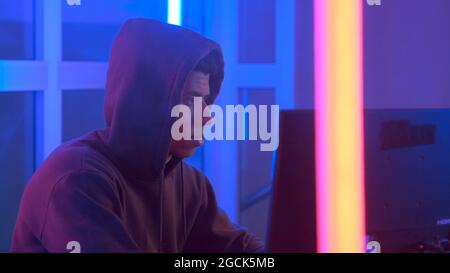 Nahaufnahme von multinationalen Hackern, die das Netzwerksystem durchdringen. Er arbeitet im dunklen Raum mit Neonlichtern. Stockfoto