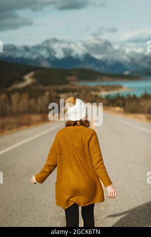 Rückansicht einer nicht erkennbaren Touristenattraktion in legerer Kleidung, die auf dem David Thompson Highway in der Nähe des abraham Sees vor verschneiten Bergen in Alberta, C, läuft Stockfoto