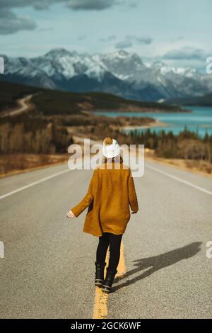 Rückansicht einer nicht erkennbaren Touristenattraktion in legerer Kleidung, die auf dem David Thompson Highway in der Nähe des abraham Sees vor verschneiten Bergen in Alberta, C, läuft Stockfoto