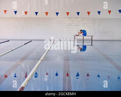 Seitenansicht des Trainers, der den Körper dehnt und die Knie umarmt, während er während des Wassergymnastik-Trainings im Pool trainiert Stockfoto