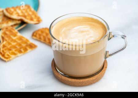 Cafe Latte und Herzwaffeln auf Marmortisch im Garten des Cafés Stockfoto