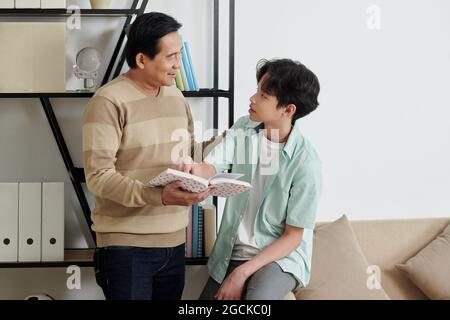 Positiver Vater und Sohn stehen im Regal und diskutieren neues Buch Stockfoto