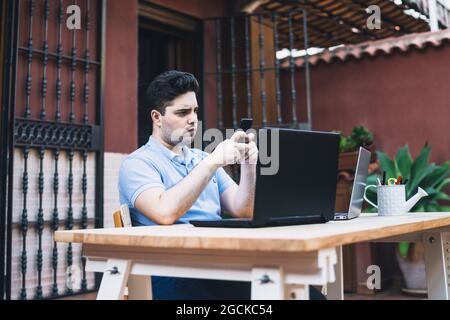 Mann, der ein Mobiltelefon benutzt, während er mit Laptops arbeitet, die Kryptowährungen im Freien handeln Stockfoto
