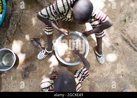 In diesem Bild teilen sich zwei kleine schwarze afrikanische Brüder in identischer Kleidung einen fleischlosen Reisteller, der auf dem Boden sitzt, mit ihrem rechten han Stockfoto