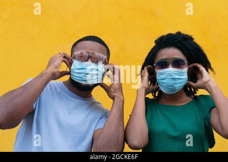 Schwarzes Paar mit Maske, die auf gelbem Hintergrund posiert und die Kamera anschaut Stockfoto