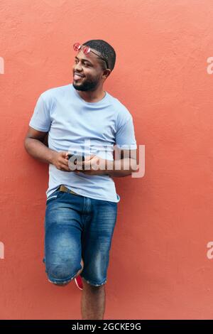 Lächelnder afrikanischer Mann mit einem Smartphone, das wegschaut, während er in der Stadt steht Stockfoto