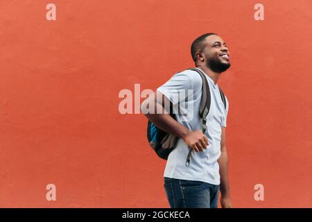Lächelnder schwarzer Mann mit Rucksack, der im Freien aufschaut Stockfoto