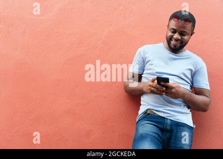 Lächelnder afrikanischer Mann, der in der Stadt auf sein Smartphone schaut Stockfoto