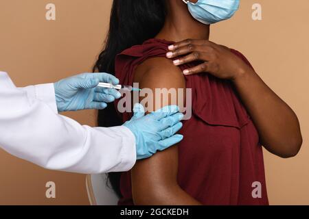 Nahaufnahme der Krankenschwesternhände in medizinischen Schutzhandschuhen, die eine intramuskuläre Injektion in die Schulter bei nicht erkennbarer weiblicher Patientin vornehmen, Nahaufnahme. Vacci Stockfoto