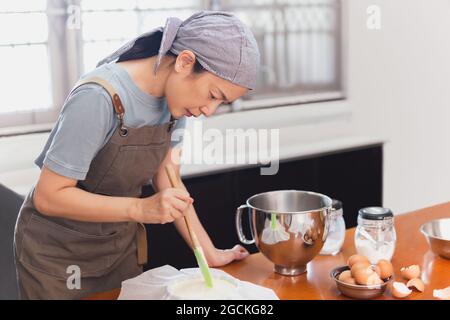 Frau Becherglas Vorbereitung Kuchen mischen Teig in Form für das Backen Form. Stockfoto