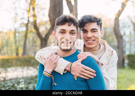 Fröhliche LBGT-Männer umarmen sich, während sie im Park stehen und die Kamera betrachten Stockfoto