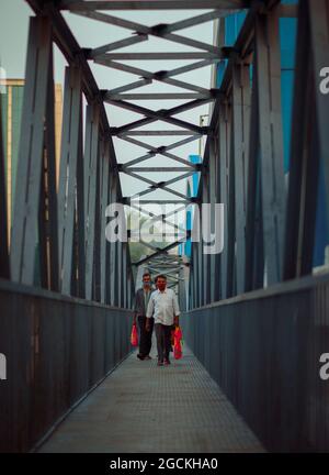 Männer gehen mit einer Tasche in der Hand durch eine Brücke zur Arbeit Stockfoto