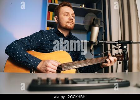 Low-Angle-Ansicht des Gitarristen Sänger Mann spielen auf akustische Gitarre Aufnahme singen Lied mit professionellen Mikrofonständer im Heimstudio. Stockfoto