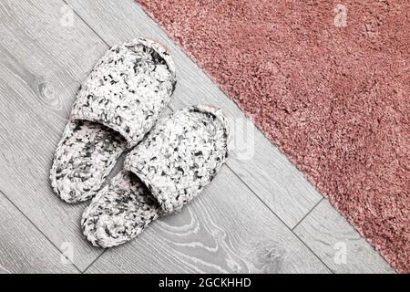 Weiße Strickschuhe stehen auf einem grauen Holzboden auf einem rosa Teppich, Draufsicht Stockfoto