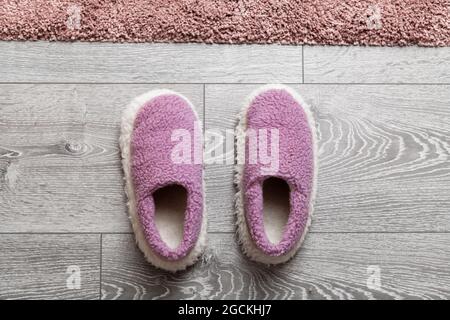 Kuschelige Wollschuhe stehen auf einem grauen Holzboden vor einem rosa Teppich Stockfoto