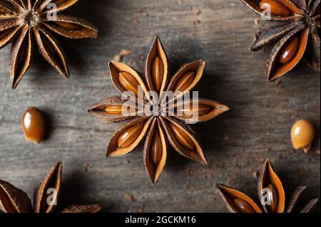 Nahaufnahme von aromatischen getrockneten Anissternen mit Samen auf rustikalem Holztisch verstreut für Gastronomie-Konzept Hintergrund Stockfoto