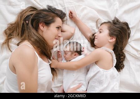 Von oben lächelnde Mutter und kleines Mädchen liegen auf dem Bett mit niedlichen Säugling Stockfoto