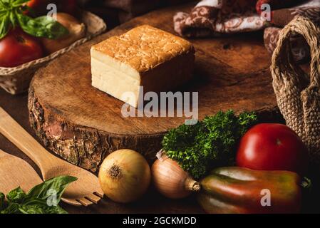 Halbweichen Käse zwischen frischen Tomaten und Zwiebeln auf dem Tisch mit Spatel und lockiger Petersilie schneiden Stockfoto