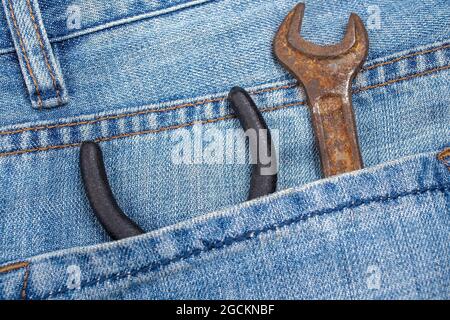 Rostiger Schraubenschlüssel und eine Zange befinden sich in der Gesäßtasche der Jeans. Werkzeug in spezieller Arbeitskleidung. Nahaufnahme. Stockfoto