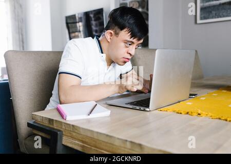 Focus Latin Teenager Junge mit Down-Syndrom Surfen Netbook, während am Tisch sitzen und online von zu Hause aus studieren Stockfoto