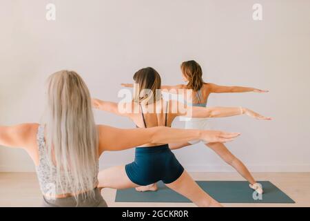 Rückansicht von nicht erkennbaren Frauen, die während des Gruppenunterrichts im Studio Yoga in Virabhadrasana praktizieren Stockfoto