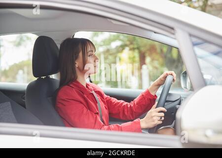 Durch das Fenster Seitenansicht der selbstbewussten jungen Frau in roter Jacke fahren moderne Automobil in der Stadt Stockfoto