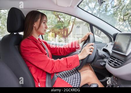 Durch das Fenster Seitenansicht der selbstbewussten jungen Frau in roter Jacke fahren moderne Automobil in der Stadt Stockfoto