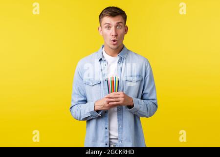 Hobbys, Freizeit und Menschen Lifestyle-Konzept. Aufgeregt und fasziniert junger Mann zu lernen, wie man zeichnet, halten Buntstifte und suchen mit Stockfoto