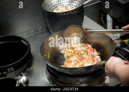 Hoher Winkel der Ernte anonymen Koch braten Reis mit Gemüse im Wok während Kochen Gericht mit Garnelen in der Küche des Restaurants Stockfoto