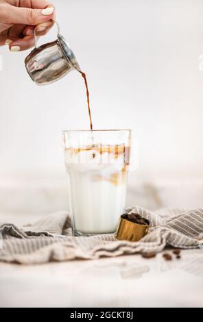 Weibliche Hand gießt Espresso und macht Iced Latte Kaffee Stockfoto