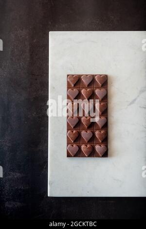 Draufsicht auf köstliche Schokoladen-Bonbons mit Nüssen in Herzform auf Marmortablett auf Tischhintergrund Stockfoto