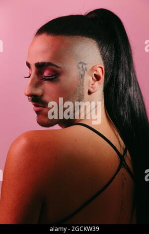 Seitenansicht Porträt der glamourösen Transgender bärtigen Frau in raffiniertem Make-up posiert mit geschlossenen Augen vor rosa Hintergrund im Studio Stockfoto