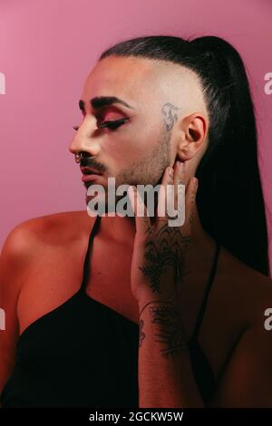 Seitenansicht Porträt der glamourösen Transgender bärtigen Frau in raffiniertem Make-up posiert mit geschlossenen Augen vor rosa Hintergrund im Studio Stockfoto