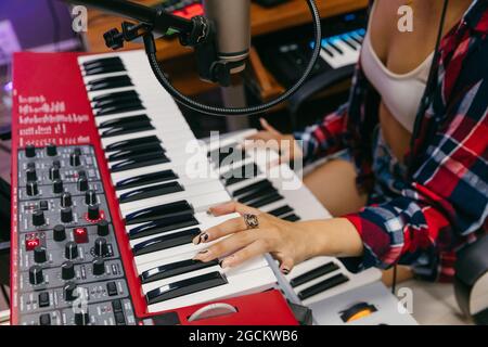 Beschnitten nicht erkennbare afroamerikanische Sängerin im Headset spielen Synthesizer, während Song ins Mikrofon im Aufnahmestudio Stockfoto