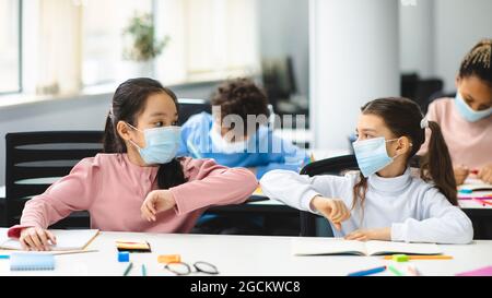 Verschiedene Schüler tragen Gesichtsmasken Begrüßung und stoßen Ellbogen Stockfoto