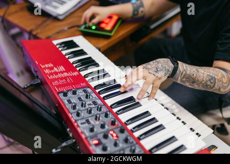 Crop unkenntlich tätowierten männlichen Pianisten, der moderne Synthesizer spielt, während er am Schreibtisch im Aufnahmestudio Musik komponiert Stockfoto