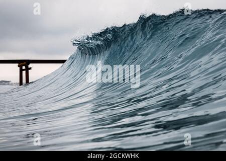 Krachende glasige Welle am Strand. Brechende Meereswelle und alter Pier Stockfoto