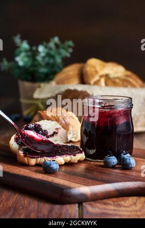 Die Vorbereitung des Frühstücks der Croissants mit der Heidelbeermarmelade auf dem hölzernen Tisch Stockfoto