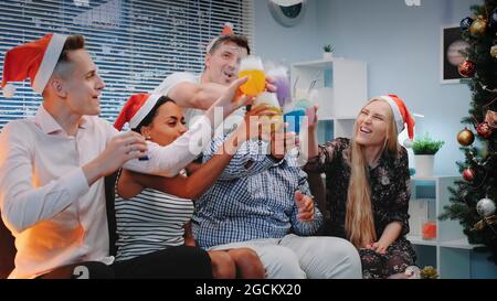 Eine Gruppe gemischter Rennfreunde, die Weihnachten im Konfettiblasen feiern, während sie zu Hause Jubeleien und Partypfeifen machen. Stockfoto