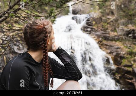 Seitenansicht einer unkenntlich nachdenklichen Wandererin, die auf den Hintergrund eines Wasserfalls im Wald der Pyrenäen blickt Stockfoto