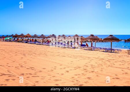 Strohschirm Sonnenschirmen mit Menschen Sonnenbaden auf Sonnenliegen Sandstrand am strand praia rosa branca Quarteira Quarteira Algarve Portugal Stockfoto