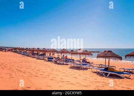 Strohschirm Sonnenschirmen mit Menschen Sonnenbaden auf Sonnenliegen Sandstrand am strand praia rosa branca Quarteira Quarteira Algarve Portugal Stockfoto