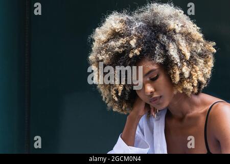 Nachdenkliche afroamerikanische Frau, die ein stilvolles, legeres Outfit trägt und gegen eine farbenfrohe Tür steht Stockfoto