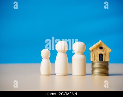 Drei Holzfiguren Menschen, die in der Nähe eines winzigen Holzhauses auf Münzen stehen. Konzept für Familie, Darlehen, Immobilienleiter, Finanzen, Hypothek, Echt Stockfoto