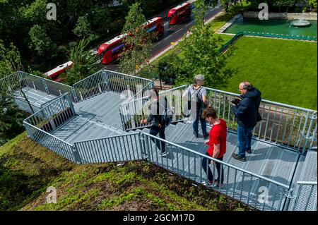 London, Großbritannien. 9 August 2021. Der Blick von oben nach Westen, wo die Baustelle durch einen frischen Rasen ersetzt wurde - den £2 Million Marble Arch Mound - wurde im Februar angekündigt und wurde gerade im August nach einem „Fehlstart“ kostenlos wieder eröffnet. Besucher können auf den 25 Meter hohen Gipfel klettern, von dem aus man von einer Aussichtsplattform aus einen 360-Grad-Blick auf die Oxford Street und den Hyde Park hat und von der breiten Öffentlichkeit nie zuvor gesehene Ausblicke genießen kann. Auf dem Weg nach unten steigen die Besucher in einen ausgehöhlten Raum, der für Ausstellungen genutzt wird. Es ist bis zum 2022. Januar für Besucher geöffnet.“ Entworfen von der niederländischen Firma Stockfoto